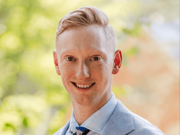 White male with blonde hair. He is wearing a blue suit. He is smiling.